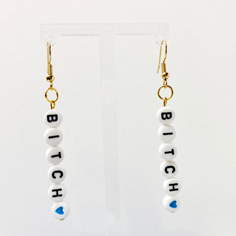 Hanging earrings with white beads with black letters spelling bitch with a heart bead. 