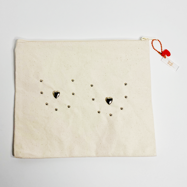 Canvas pouch bedazzled with silver metal studs to outline the shape of breasts with metal hearts for the nipples. The pouch is on a white background.